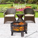 Gardebruk vuurkorf met vlammen, in een tuin met twee stoelen, een bijzettafel en een achtergrond van bloemen.