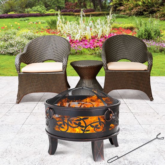 Gardebruk vuurkorf met vlammen, in een tuin met twee stoelen, een bijzettafel en een achtergrond van bloemen.