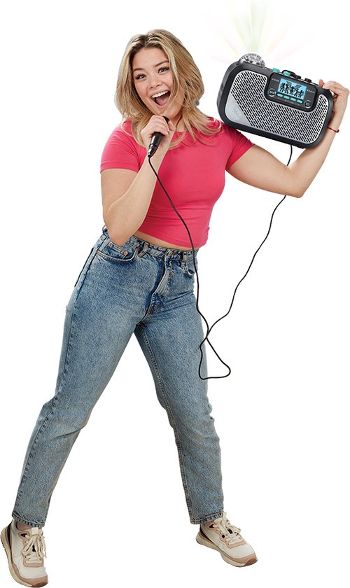 Vrolijke jonge vrouw met roze top en spijkerbroek zingt in microfoon bij zwarte VTech Super Sound Karaoke speaker.