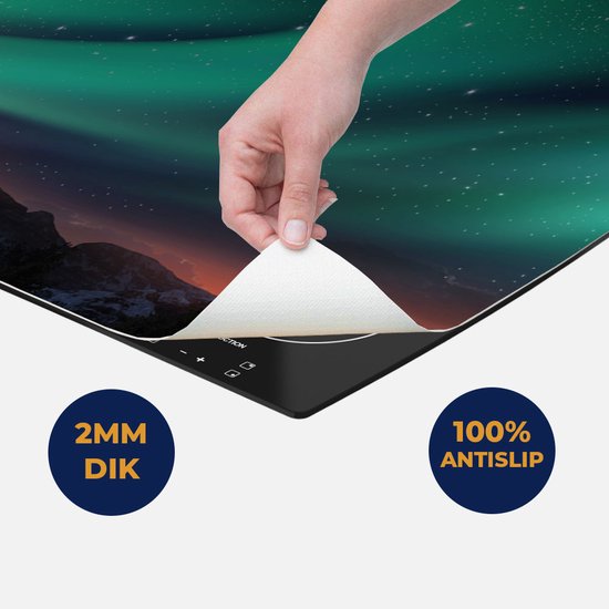Een hand trekt de beschermfolie van een mat met Noorderlicht-afbeelding, geplaatst op een inductiekookplaat.