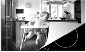 KitchenYeah® Inductie beschermer 80.2x52.2 cm - Baby in kinderstoel aait een hond - zwart wit - Kookplaataccessoires - Afdekplaat voor kookplaat - Inductiebeschermer - Inductiemat - Inductieplaat mat