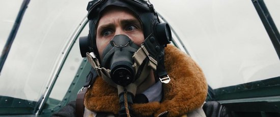 Close-up van een mannelijke piloot in een cockpit, met een vliegmasker en een bruine bontkraag, kijkend met grote ogen.