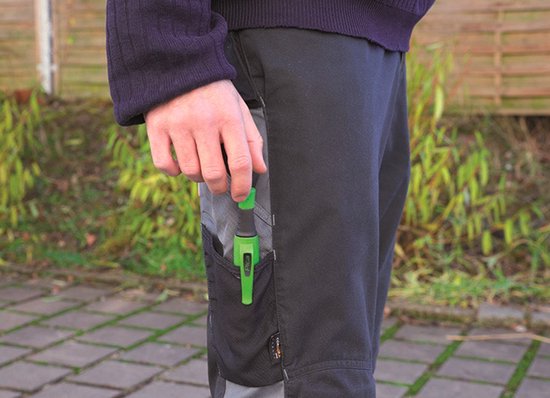 Mannelijke hand met groene markeerstift in het werkbroekvak. Zwarte en grijze werkbroek.