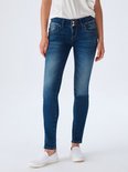 Model in een witte top en donkerblauwe skinny jeans met een lichte wassing en distress details.
