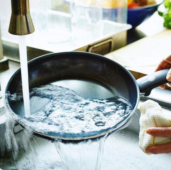 Een pan wordt in een gootsteen afgespoeld onder stromend water.