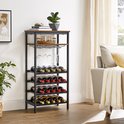 Een donkerbruin metalen wijnrek met houten bladen, een glazenrek en plaats voor 20 flessen, in een woonkamer met een bank en plant.