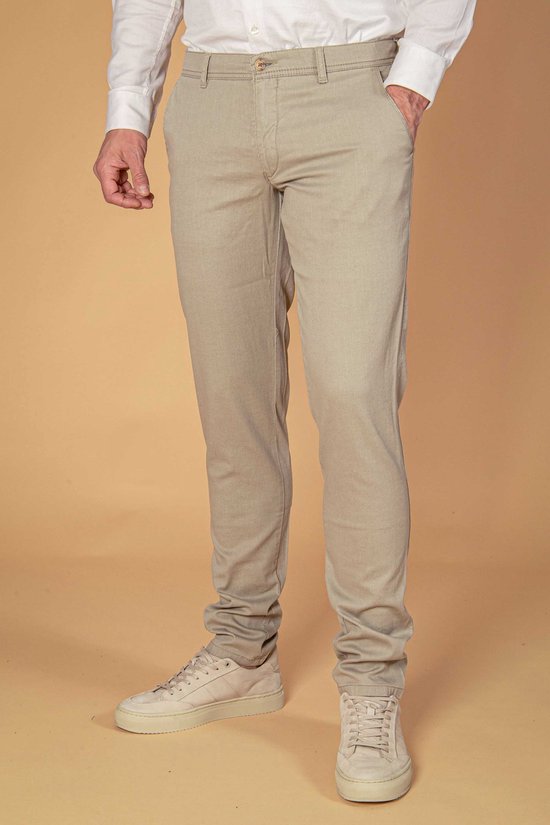 Model draagt een kaki chino gecombineerd met een wit overhemd en beige sneakers.