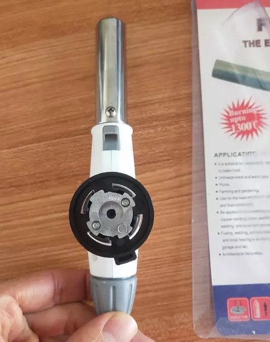Onderkant van de witte gasbrander met zilveren buis en grijze draaiknop, vastgehouden in een hand.