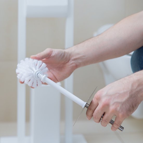 Een persoon verwisselt de witte borstelkop van een toiletborstel. De schacht is van metaal.