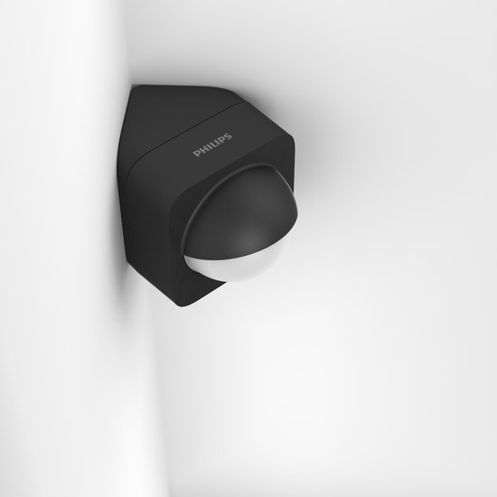 Zwarte Philips Hue buitenbewegingssensor met 'PHILIPS' logo, in een hoek op een witte achtergrond.