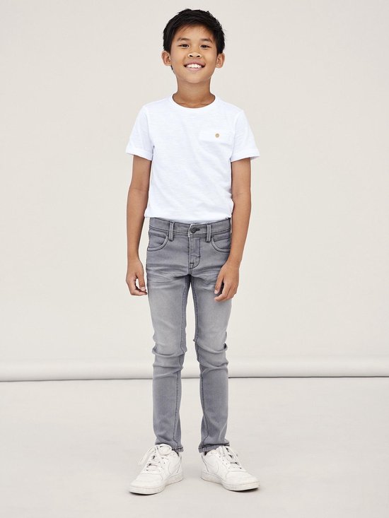 Jongetje in een witte T-shirt en strakke, grijze jeans.