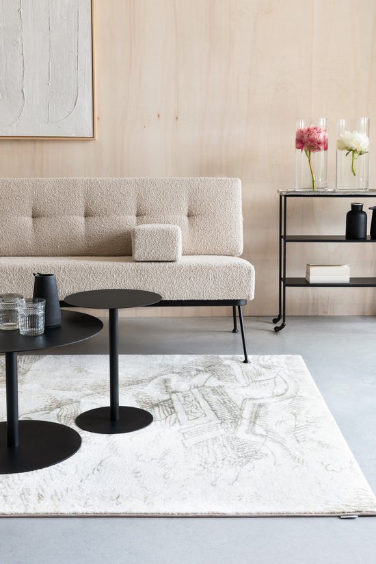 Een beige bouclé bank staat in een woonkamer naast een salontafel met zwarte vazen.