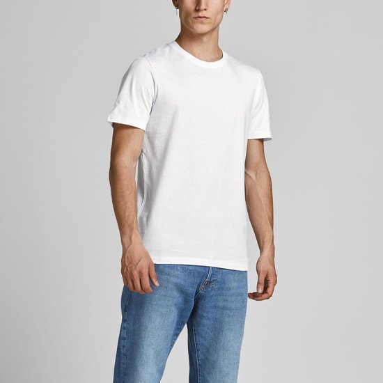 Man in een wit T-shirt en blauwe spijkerbroek, staand naar de zijkant gedraaid.