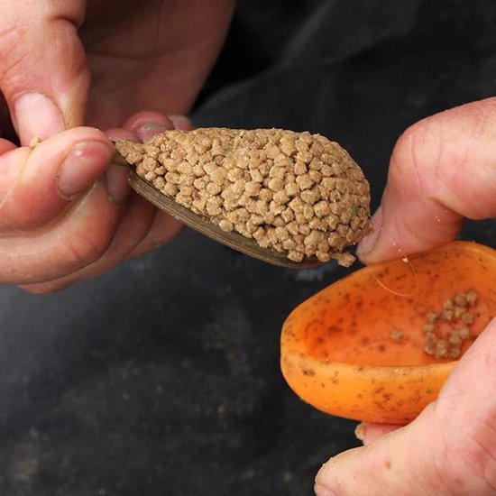 Des mains remplissent un amorceur vert d'appâts, avec un moule orange à côté.