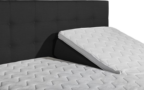 Close-up van een zwart, gestoffeerd hoofdbord en een wit, ruitvormig gestikt matras op een verstelbaar boxspringbed.