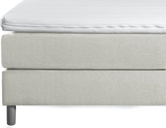 Dichtbij weergave van een beige boxspring met gestreept matras en witte topper.