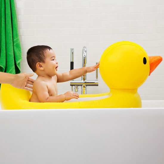 Baby in een geel opblaasbaar badeendje badje, met handjes op de rand.