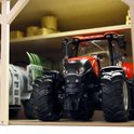 Close-up van een rode tractor in een houten landbouwloods, naast een grijze tank met aanhanger.