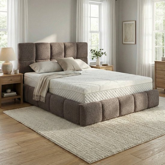 Un sommier taupe rembourré avec une tête de lit capitonnée et un matelas blanc à motif subtil. Posé sur un tapis clair.