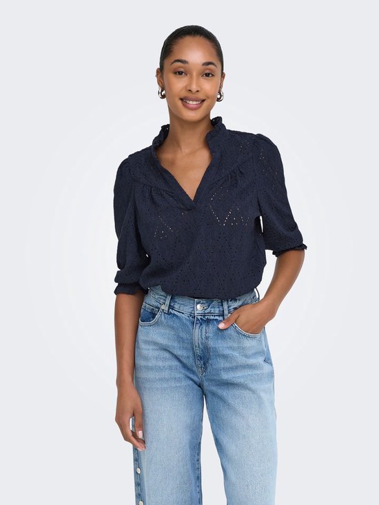 Model draagt donkerblauwe top met kanten details, pofmouwtjes en een opstaande kraag, gecombineerd met jeans.