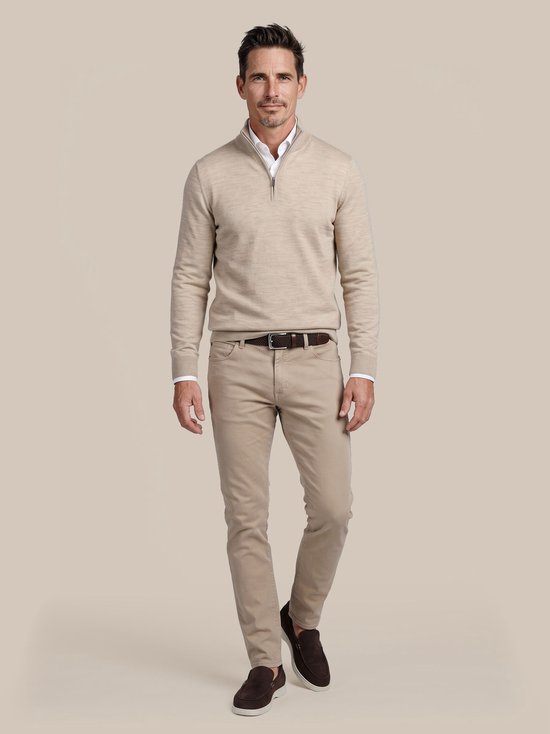 Een man draagt een beige chino broek met een beige trui, witte blouse en donkerbruine riem.