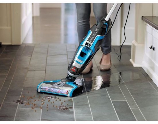 Vrouw met blauwe BISSELL CrossWave stofzuiger op grijze tegels.