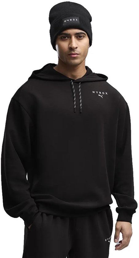 Man met zwarte hoodie met capuchon, een logo op de borst en zwarte muts.