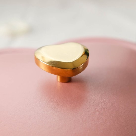 Gouden knop in hartvorm op een roze gietijzeren braadpan.