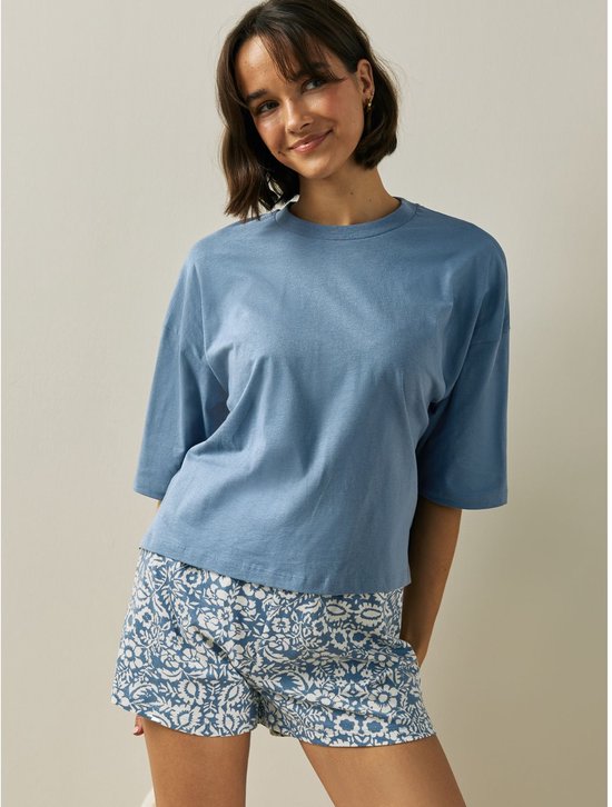 Model met blauw t-shirt en korte pyjamabroek met bloemenprint.