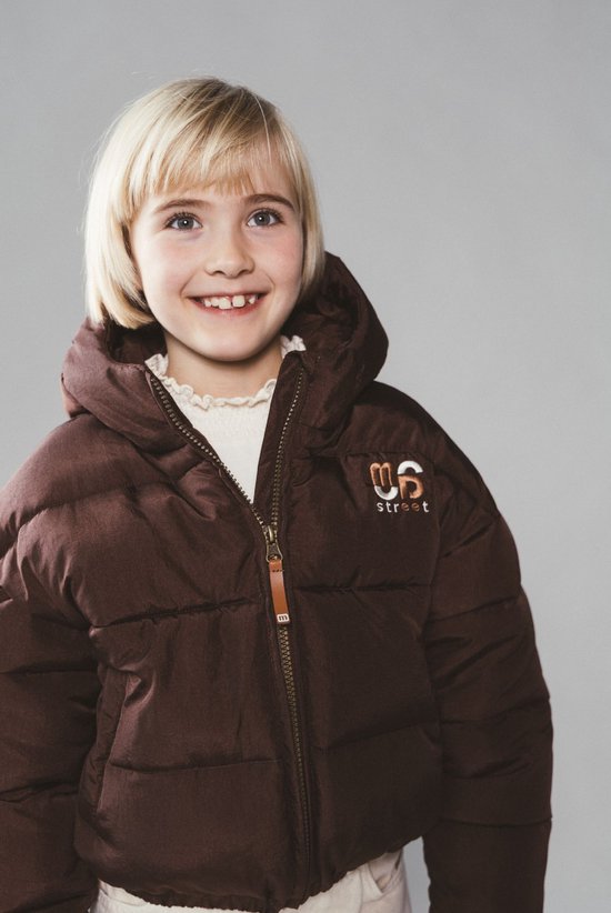 Close-up van een kind in een bruine pufferjas met "Moodstreet" logo op de borst.