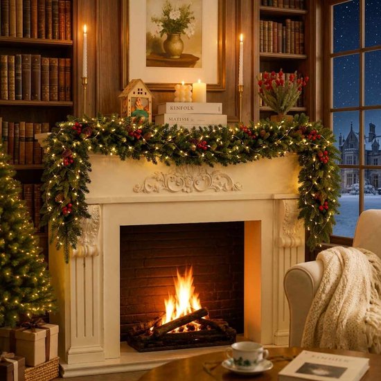 Verlichte kerstguirlande met dennenappels en bessen versiert een schouw in een kamer met een haardvuur en boeken.