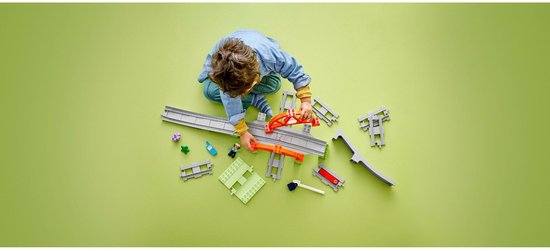 Kind speelt met LEGO DUPLO treinrails, brug en accessoires op groen vlak.