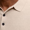Detail van de kraag en knoopsluiting van een lichtbeige gebreid poloshirt met twee zwarte knoopjes.