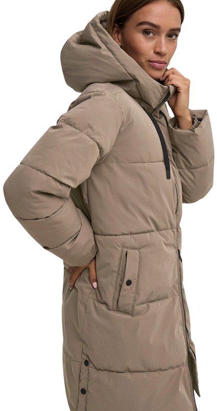 Bruine, lange winterjas met capuchon, gedragen door een model, hand bij de nek.