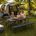 Familie eet buiten bij een campingtafel met bankjes, met een tent en fietsen op de achtergrond.