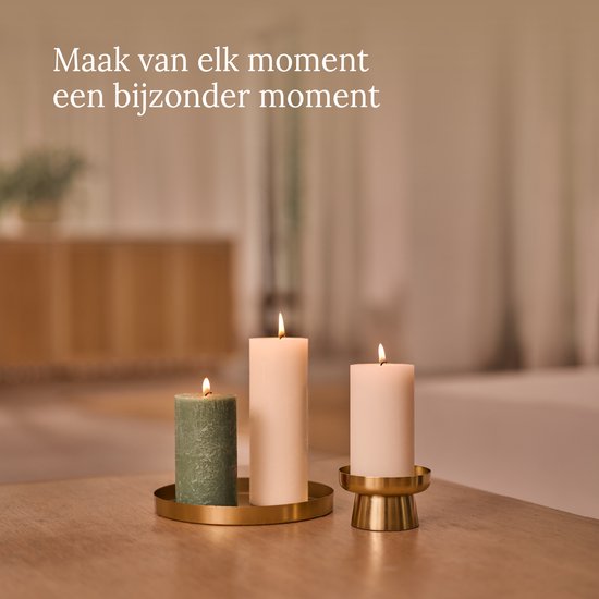 Drie brandende kaarsen op een tafel, twee ivoorkleurige en één groen.