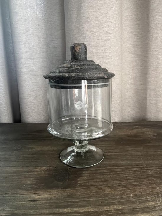 Glazen pot op voet met donker, verweerd deksel.
