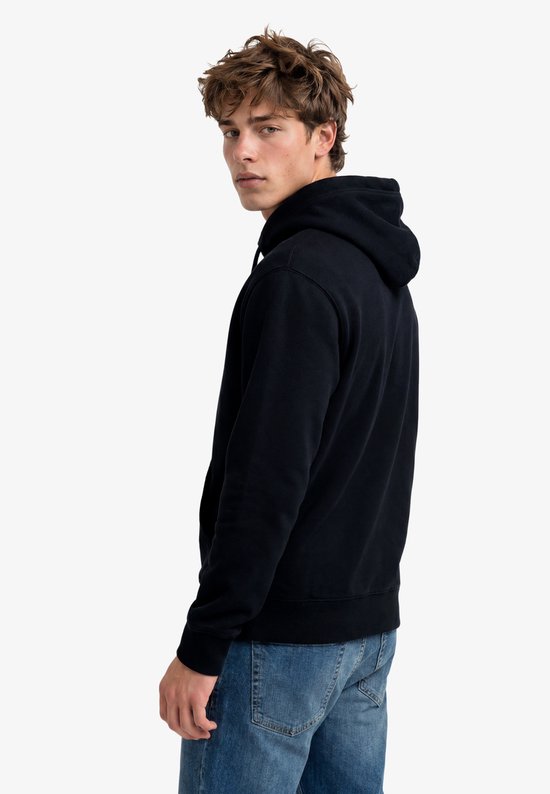 Model van achteren gezien met donkerblauwe hoodie met capuchon en jeans.