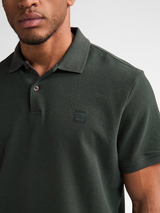 Detail van donkergroen poloshirt met gebreide stof en donker logo op borst.
