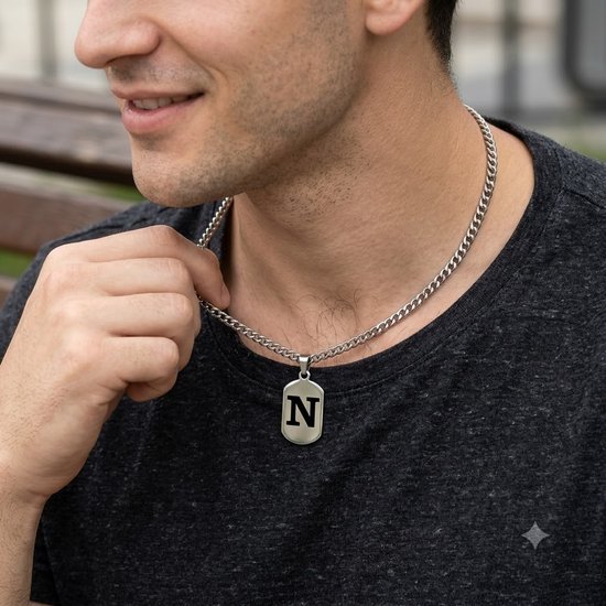 Man draagt een zilverkleurige schakelketting met een rechthoekige hanger met de letter N.