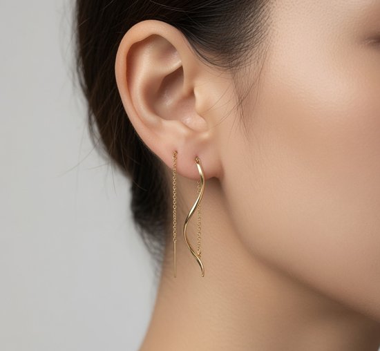 Model draagt gouden, golvende spiraal threader oorbellen met fijne gouden kettingen.