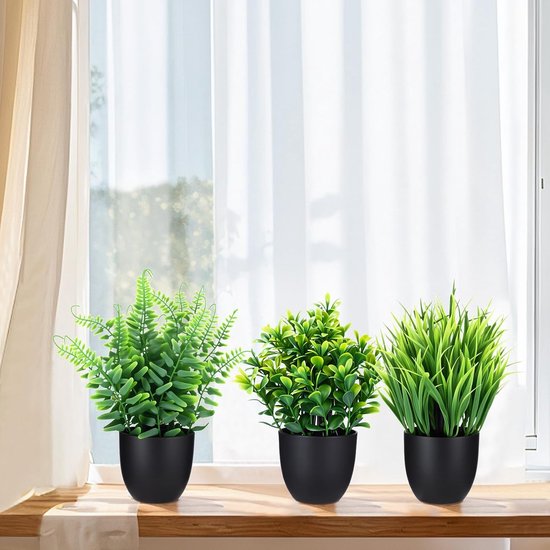 Drie kunstplanten in zwarte potten op een vensterbank voor een wit gordijn.