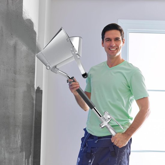 Lachende man in een groene T-shirt met een zilverkleurige mortelspeuit naast een gespoten muur.