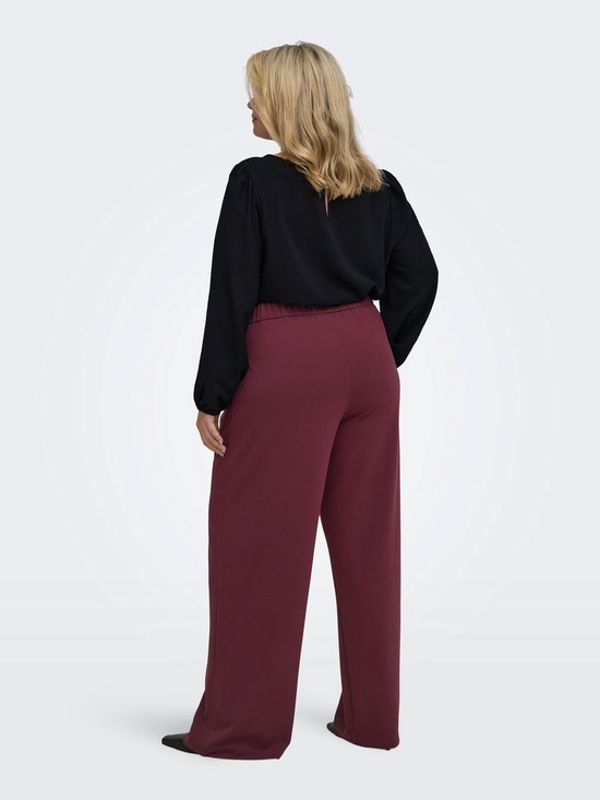 Vrouw met lange zwarte blouse en bordeauxrode wijde broek, van achteren gezien.