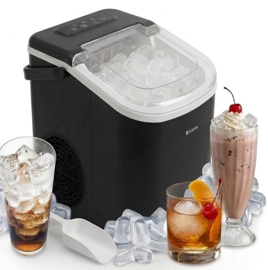 Zwarte ijsblokjesmachine van BluMill met transparant deksel, vol met ijsblokjes. Naast de machine staan een ijschep en twee glazen met drankjes en ijs, waaronder een cocktail met kers en slagroom.