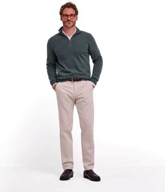 Model in een groene FALKE trui met rits, beige broek, bruine riem en mocassins.