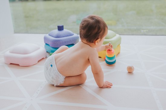 Een baby op handen en knieën, spelend met een stapeltoren. De baby draagt een 'Woosh' luierbroekje.