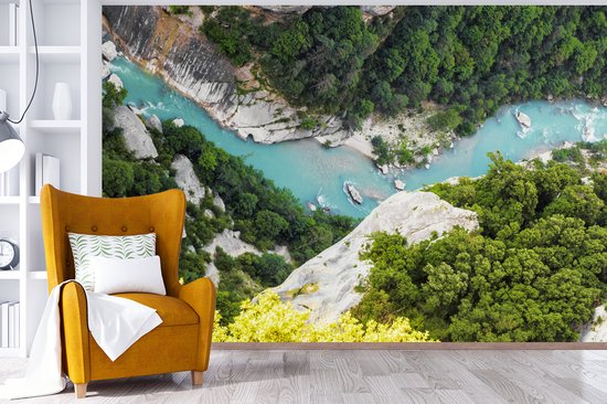 Vue d'un canyon avec une rivière bleu vif et des arbres verts, sur une tapisserie au-dessus d'un fauteuil ocre.
