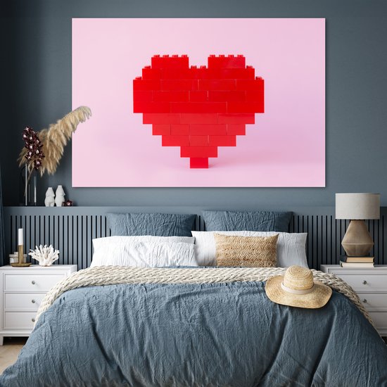 Rood hart van bouwblokken op een roze achtergrond, boven een bed met blauw beddengoed.