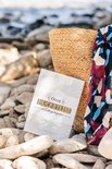 Bucketlist boek voor liefdeskoppels, gelegen naast een rieten mand en een sjaal op een stenen strand.